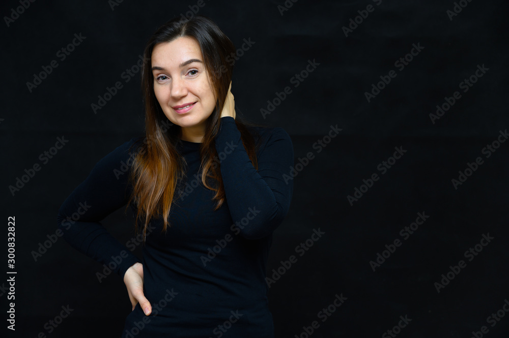Portrait of an adult woman without makeup with clean skin, with long brown hair over her face on a black background. He stands in front of the camera in a black T-shirt, shows his hands emotions. Portrait of an adult woman without makeup with clean skin, with long brown hair over her face on a black background. He stands in front of the camera in a black T-shirt, shows his hands emotions.