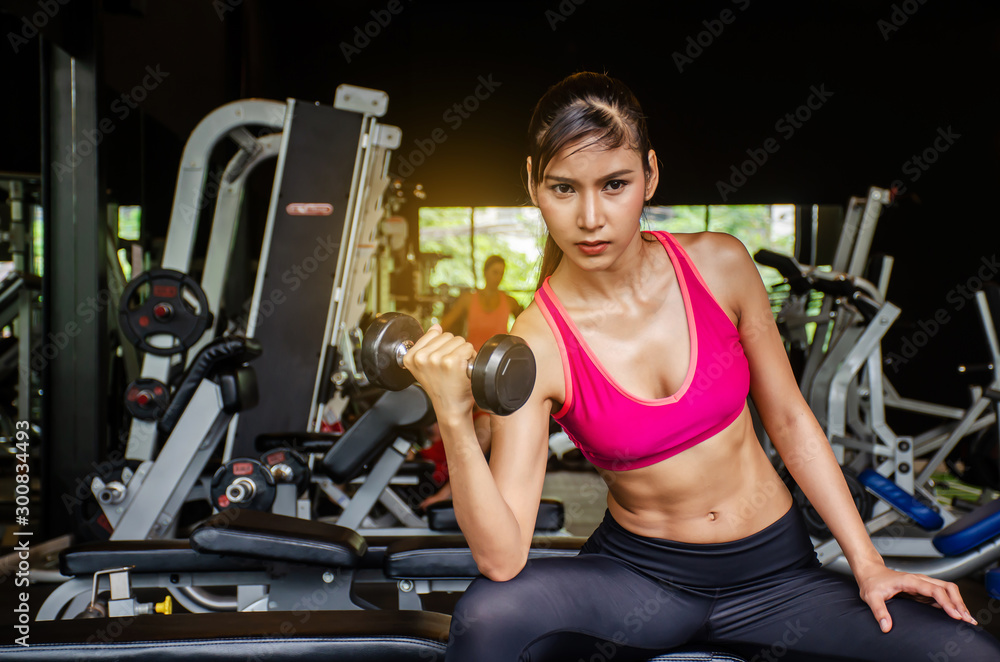 Young beautiful woman doing exercises lifting dumbbell in gym.Glad smiling girl is enjoying with her training process in the morning. She is working hard Young beautiful woman doing exercises lifting dumbbell in gym.Glad smiling girl is enjoying with her training process in the morning. She is working hard