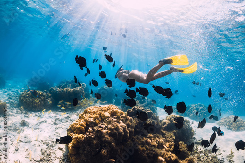 Freediver girl with yellow fins glides over sandy bottom with fishes in ocean
