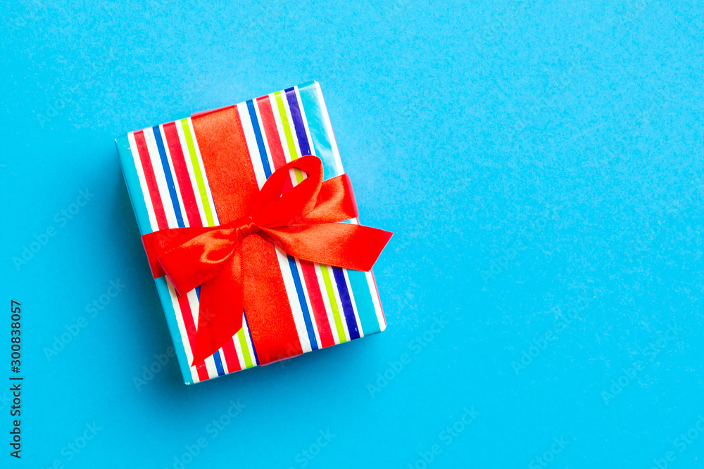 Fototapeta premium Gift box with red bow for Christmas or New Year day on blue background, top view with copy space