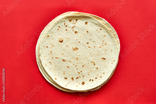 Tortillas on red background. A pile of  baked blank corn tortilla wraps on a color background with copy space. Top view or flat lay for use as a cooking, mexican restaurant or travel background. photo