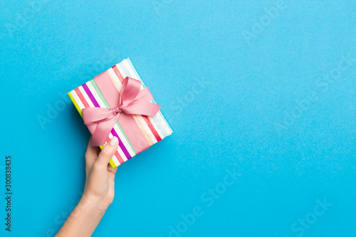 Woman arms holding gift box with colored ribbon on blue table background, top view and copy space for you design