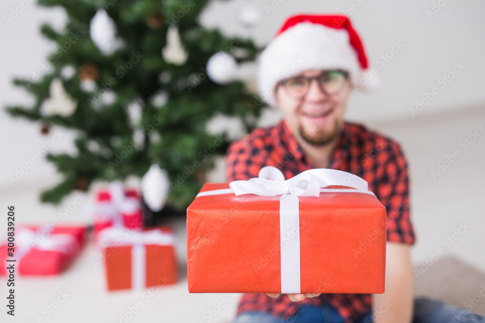 Christmas and holidays concept - Funny man in santa hat holding a gift at home in the living room Christmas and holidays concept - Funny man in santa hat holding a gift at home in the living room