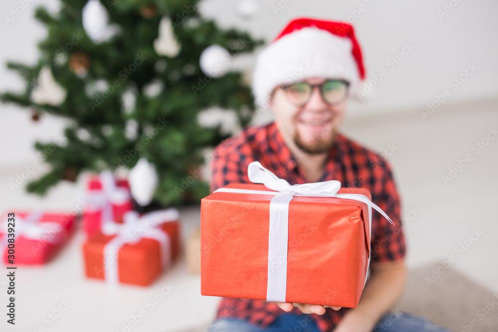 Christmas and holidays concept - Funny man in santa hat holding a gift at home in the living room Christmas and holidays concept - Funny man in santa hat holding a gift at home in the living room