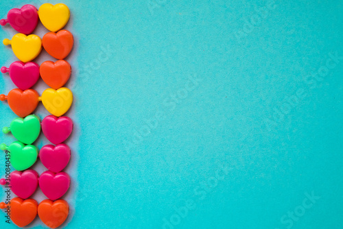 Colourful pairs of plastic hearts on left side on a blue background. Relationships. Yellow, pink, green, orange hearts. 