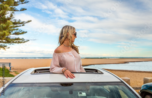 Road trip summer beach vibes.  Carefree woman in sunroof car by beach photo