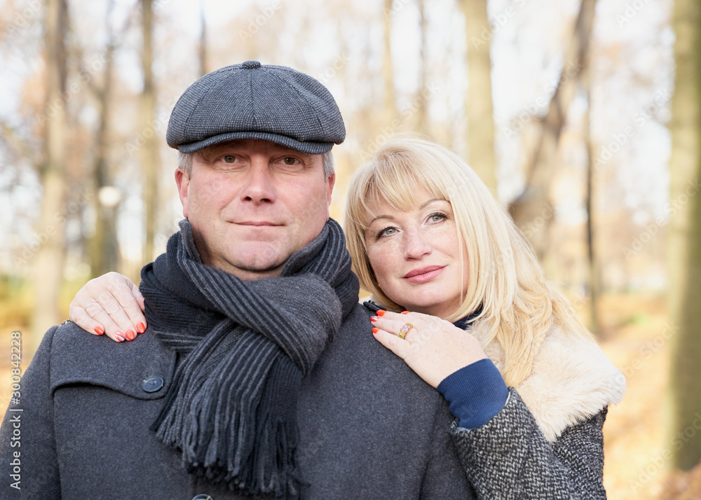 Fototapeta premium Closeup portrait of happy blonde mature woman and beautiful middle-aged brunette, looking looking directly at camera. Loving couple of 45-50 years old walks in autumn park in warm clothes