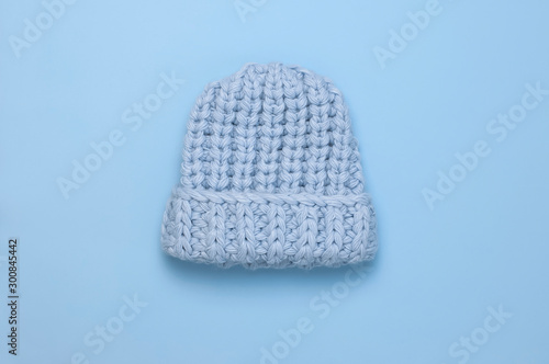 Flat lay fashionable blue knitted winter hat for women on blue background top view. Stylish woolen hat, concept of winter accessories for the cold. Advertising, shopping, winter sale