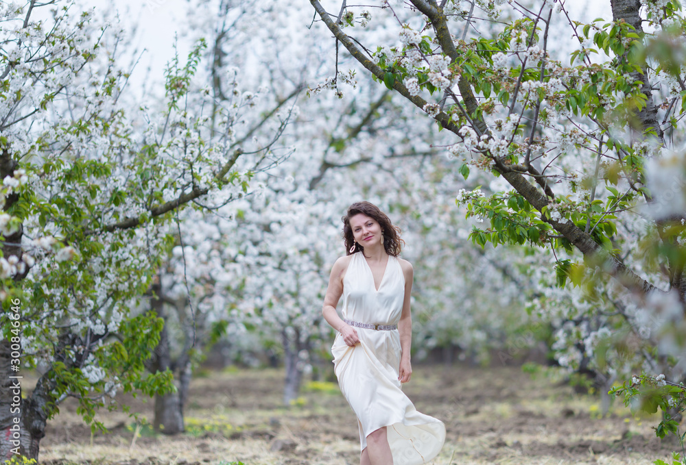 A beautiful young Caucasian woman with curly dark hair walking in blossoming orchard A beautiful young Caucasian woman with curly dark hair walking in blossoming orchard