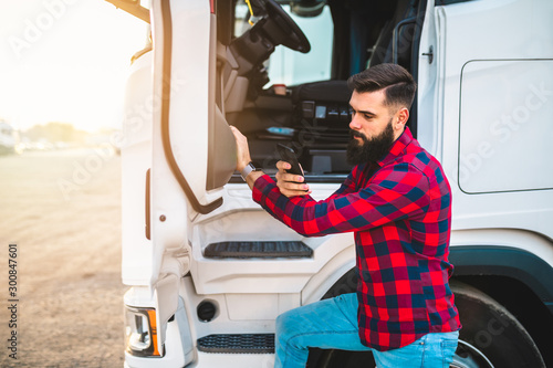 Young handsome bearded man standing in font of his truck and using phone.