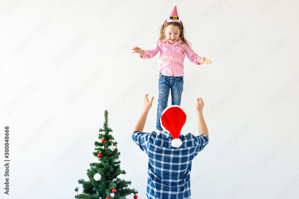 Christmas, holidays and fatherhood concept - Funny dad wearing santa hat throws his daughter up on white background with copy space