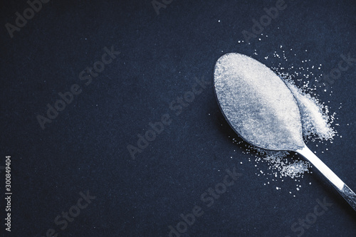 Minimalist flat lay composition sugar and spoon on the dark background. Medical, Healthcare and Diabetes Concept. Top view and selective focus.