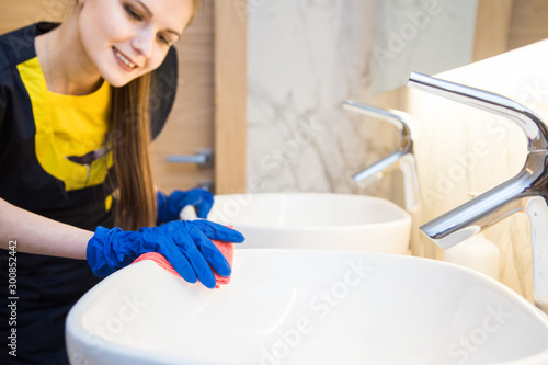 professional cleaning service. woman in uniform and gloves sponge washes the plumbing in the bathroom. Washing bath and sink