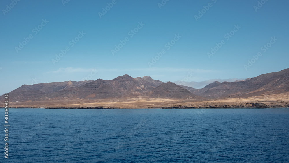 Approaching Fuerteventura island at its most southern point at Morro Jable with the display of the solitary cliffs and arid mountains behind, part of the Parque Natural Jandia, Canary Islands, Spain