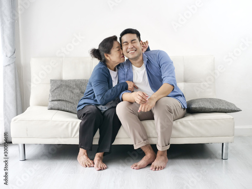 Asian mother hugging her son and sitting on sofa at home, lifestyle concept. © nuiiko