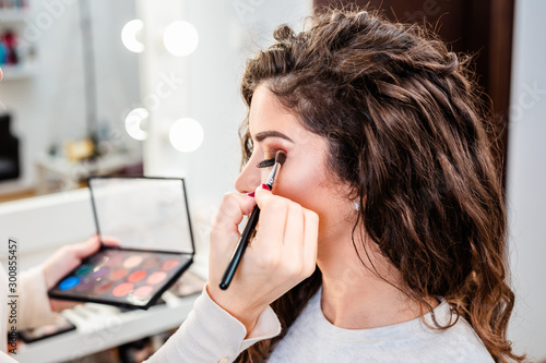 Fotografi Make up artist applying professional make up of beautiful young woman