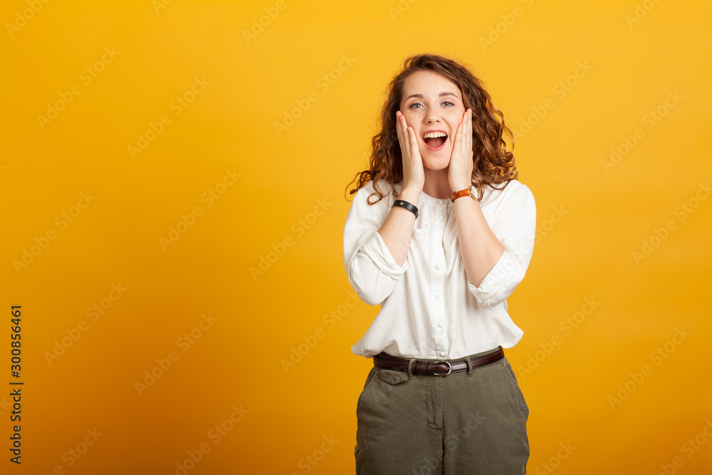 beautiful young girl surprised with open mouth holds hands on cheeks isolated on yellow background. beautiful young girl surprised with open mouth holds hands on cheeks isolated on yellow background.