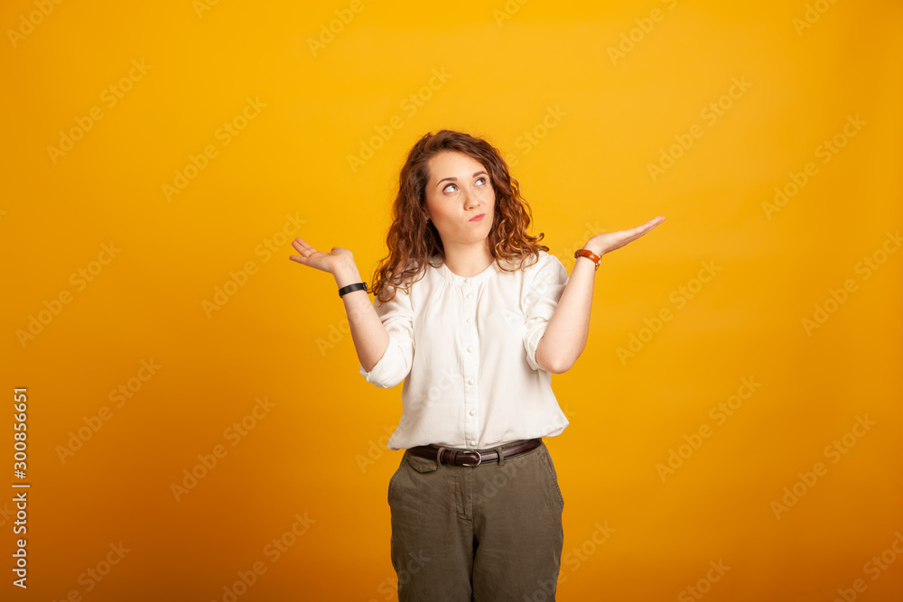 beautiful young girl chooses two items standing isolated on yellow background. beautiful young girl chooses two items standing isolated on yellow background.