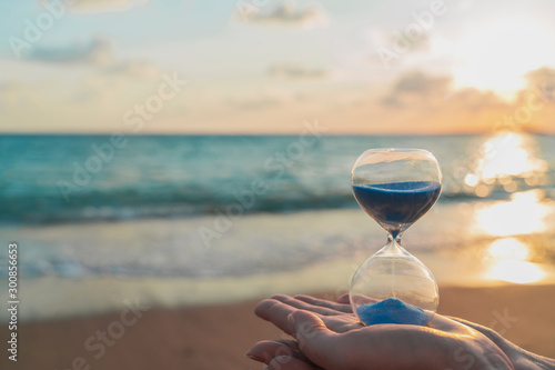 Hourglass in the hands symbolize the transience of time, which running fast. Background is seacoast and beautiful gold sunset
