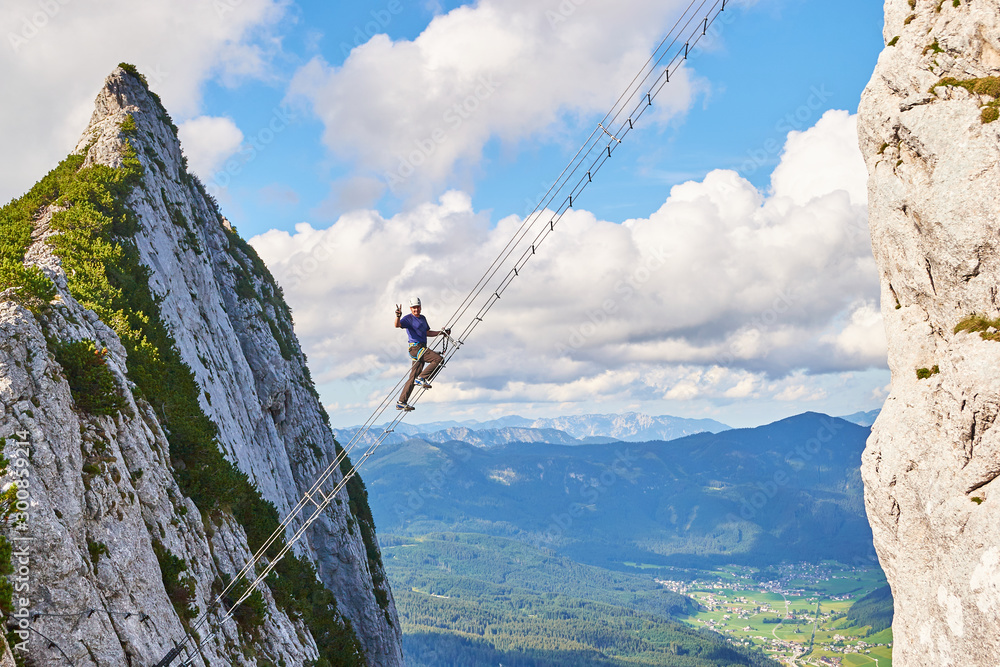 Intersport Donnerkogel via ferrata in Summer, with a man showing a victory  sign while climbing the diagonal ladder. Stairway to heaven concept. Stock  Photo | Adobe Stock