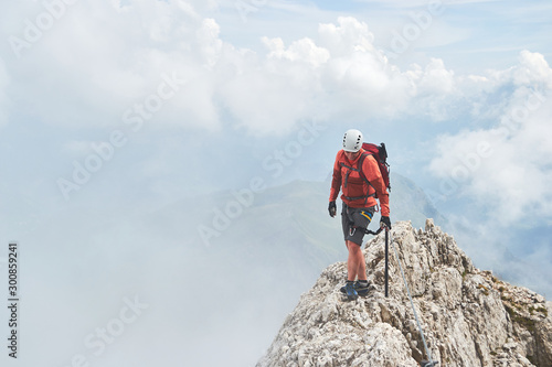 Man on a narrow mountain ridge surrounded by fog, up on via ferrata Eterna (Cadore Brigade) at Marmolada, Dolomites mountain range, Italy. Copy space on the left.