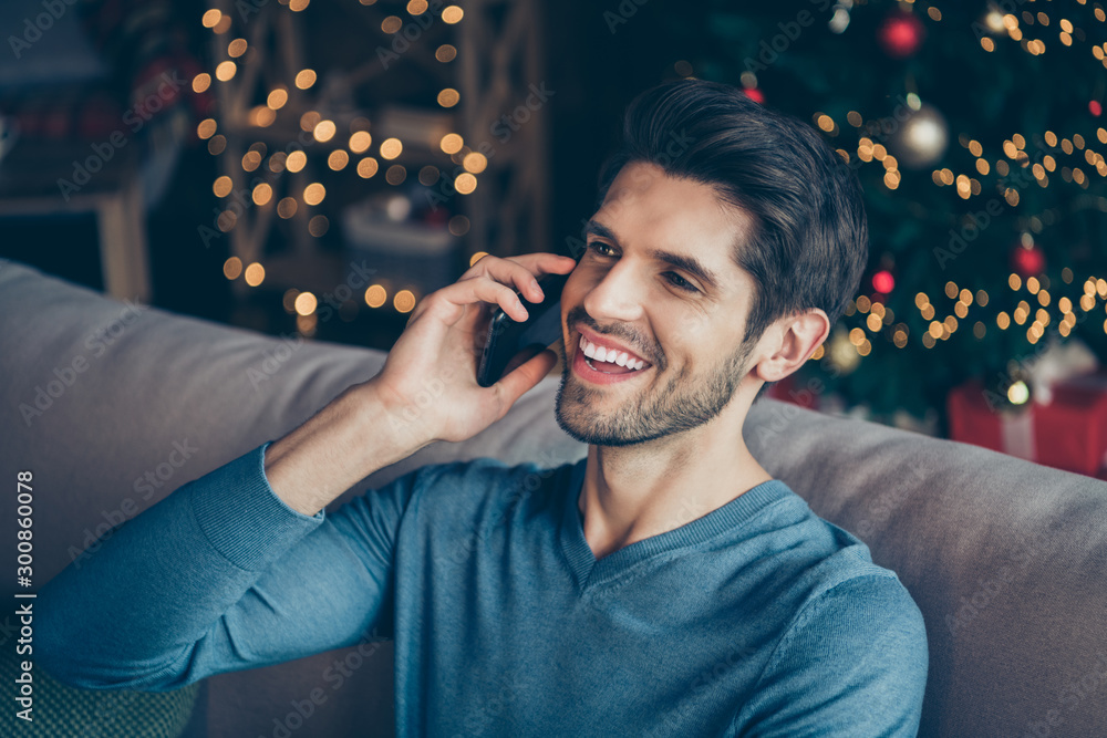Close up photo of joyful guy speaking cellphone tell congratulations with newyear enjoy christmas atmosphere sit couch in house with bright magic miracle lights - obrazy, fototapety, plakaty 