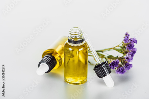 bottles of natural oil and twig of dry limonium with flowers on white background