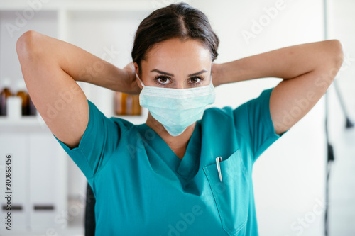 Young female doctor in medical office. Beautiful female doctor putting mask on. Close up. photo
