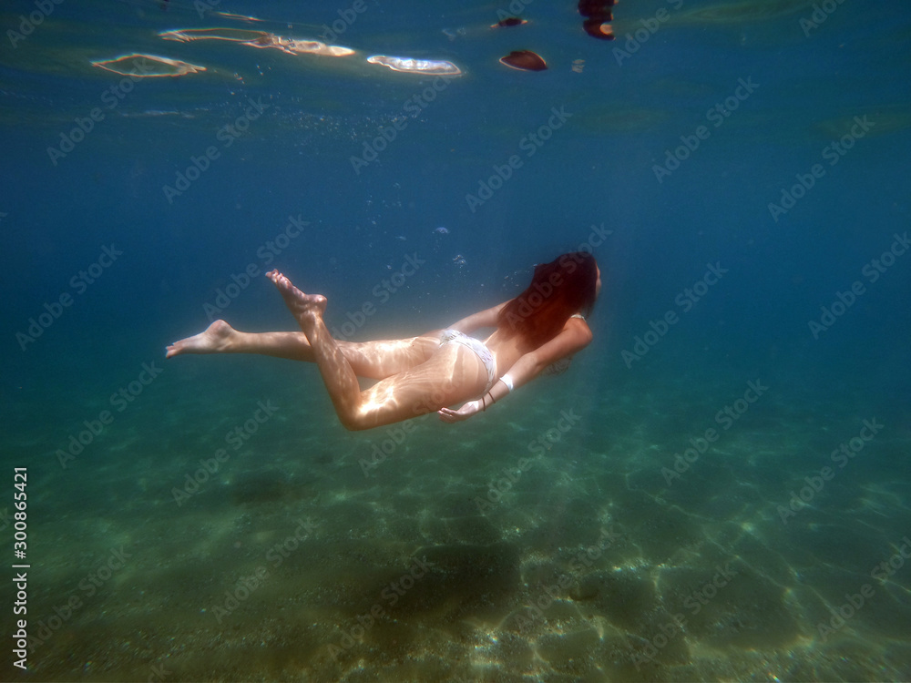 Beautiful girl in bikini swimming, floating underwater in the sea