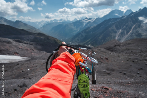 First-person view of a hand with climbing equipment high in the mountains. Mountain climbing