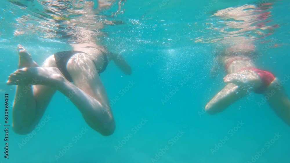Underwater view of females swimming in the blue sea, slow motion Underwater view of females swimming in the blue sea, slow motion