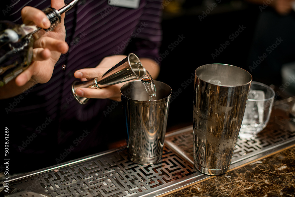 Male bartender pouring a vodka from the jigger to a steel shaker