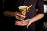 Bartender in the purple shirt serving yellow alcoholic cocktail in the glass with a dried lemon and leaf in the clothespin
