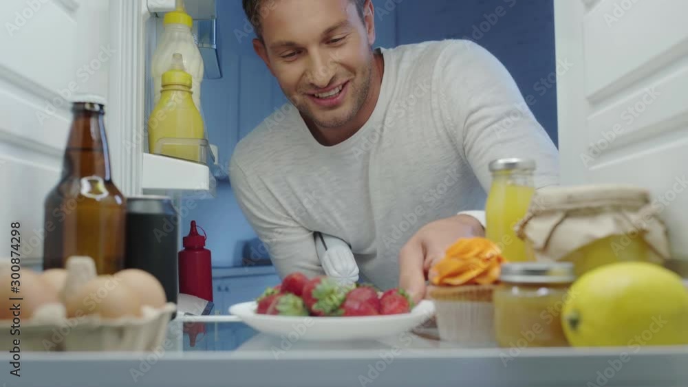 hungry man taking strawberry and container of whipped cream from fridge hungry man taking strawberry and container of whipped cream from fridge