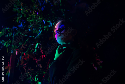  Woman in the forest lit by multicolored light - noir.