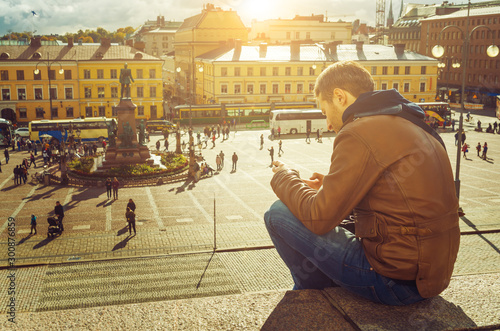 A tourist sitting in the sun and chatting on his phone in Helsinki Senate Square.