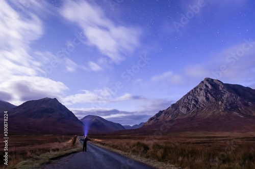 buchaille etive mor and glen etive in the argyll region of the highlands of scotland on a bright moonlit night with a person in the foreground with a bright head torch