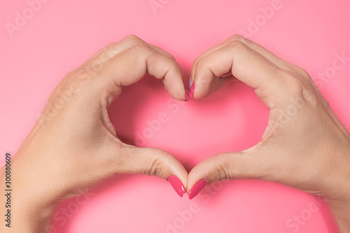 Closeup point of view photography of hands of beautiful young woman making heart gesture isolated on pastel pink background. Love and happiness concept. Nails with trendy 2 colours manicure.