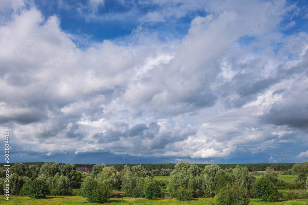 Amazing countryside landscape. Green valley, forests and blue sky with beautiful white fluffy clouds. Horizontal color photography.