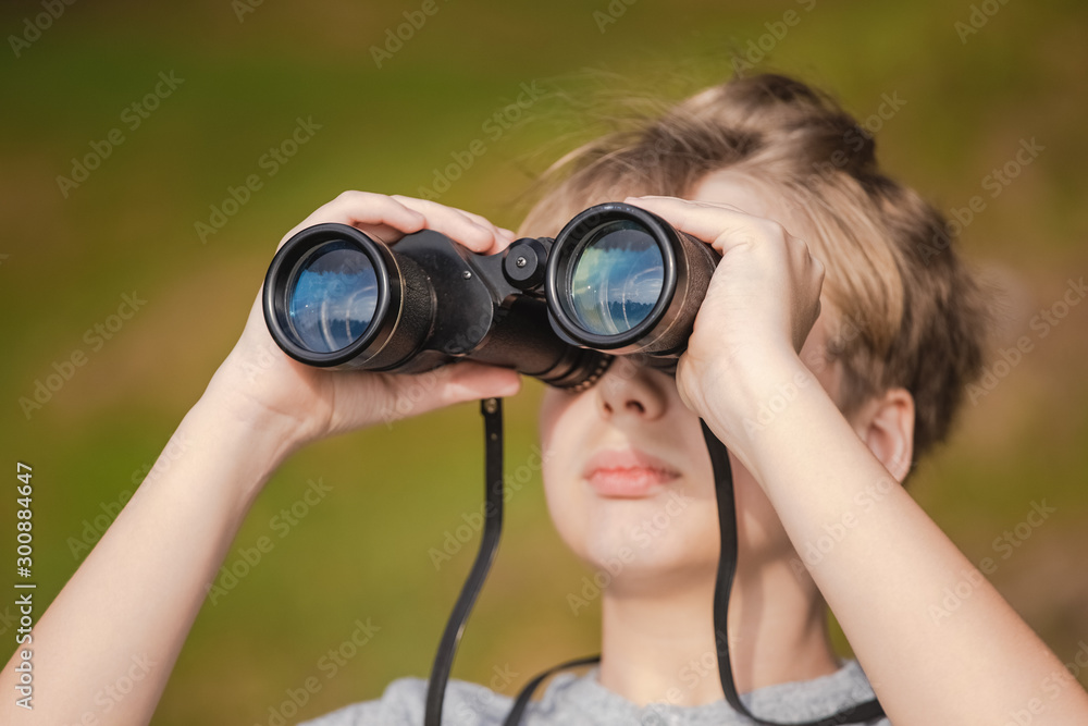 Closeup view of white clever kid looking through black binoculars standing alone outdoor. Horizontal color photography. Closeup view of white clever kid looking through black binoculars standing alone outdoor. Horizontal color photography.