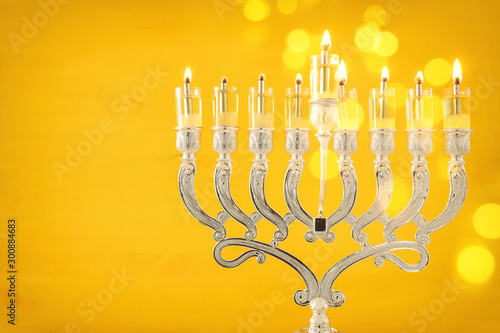 Religion image of jewish holiday Hanukkah background with menorah (traditional candelabra) and oil candles over yellow background