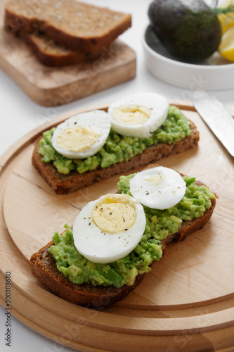 Avocado toast. Sandwich with egg, mashed on wholegrained bread on cutting board. Healthy breakfast.