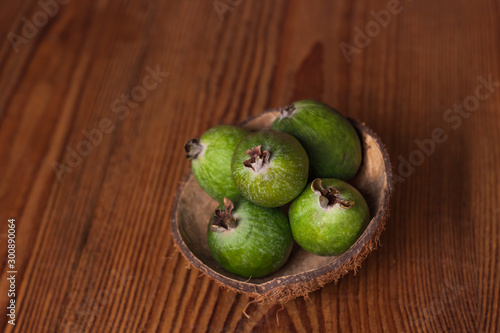 Green feijoa in a coconut shell hulf on a dark wooden background. Ripe tropical fruits, pineapple guava, raw vegan food. Low calories, rich in dietary fiber, vitamin C and B6, minerals. Copy space. photo