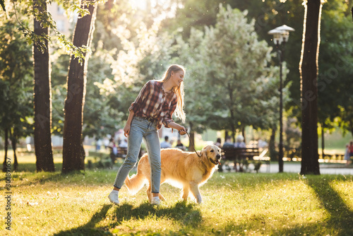 full length view of beautiful girl in casual clothes walking with golden retriever on meadow in sunlight © LIGHTFIELD STUDIOS