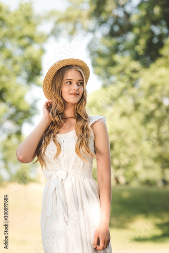 beautiful girl with straw hat standing on meadow and looking away