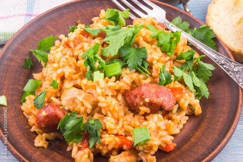 Traditional American New Orleans Jumbalaya with rice, chicken and sausages, on a clay plate, sprinkled with chopped parsley, closeup, top view. photo