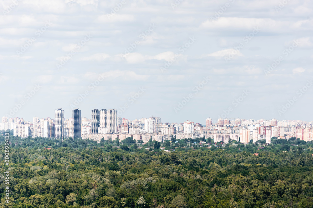 Fototapeta premium Urban scene with trees in city park, skyscrapers and buildings