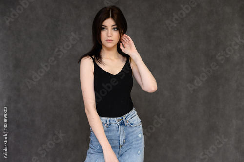 Portrait of a young pretty girl student with long black hair, on a gray background. He stands right in front of the camera, showing his hands in different poses with different emotions.