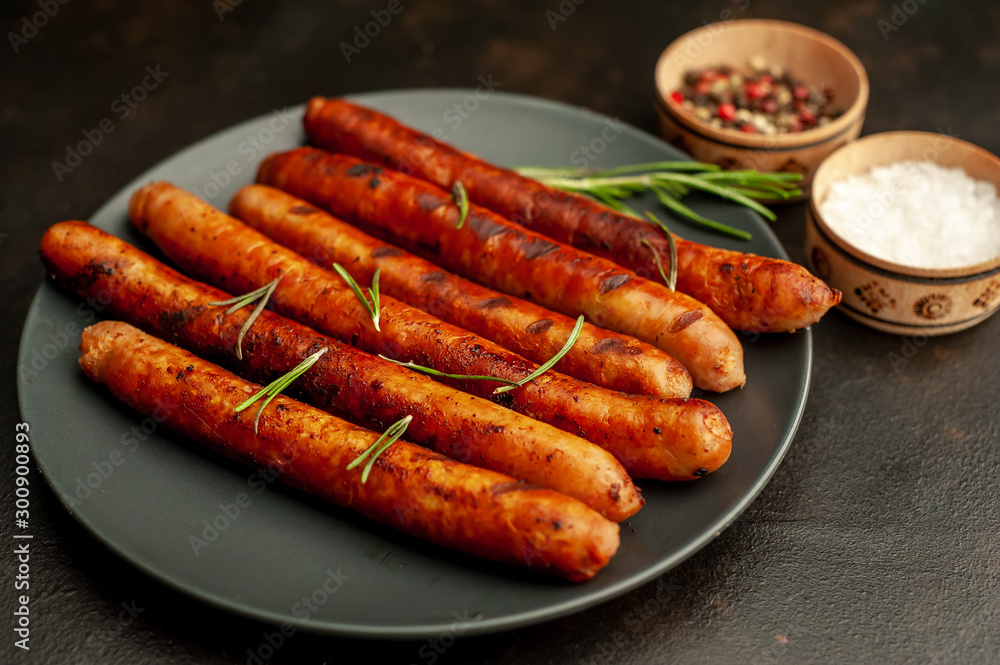 Grilled sausages on a plate with spices and rosemary on a stone table Grilled sausages on a plate with spices and rosemary on a stone table