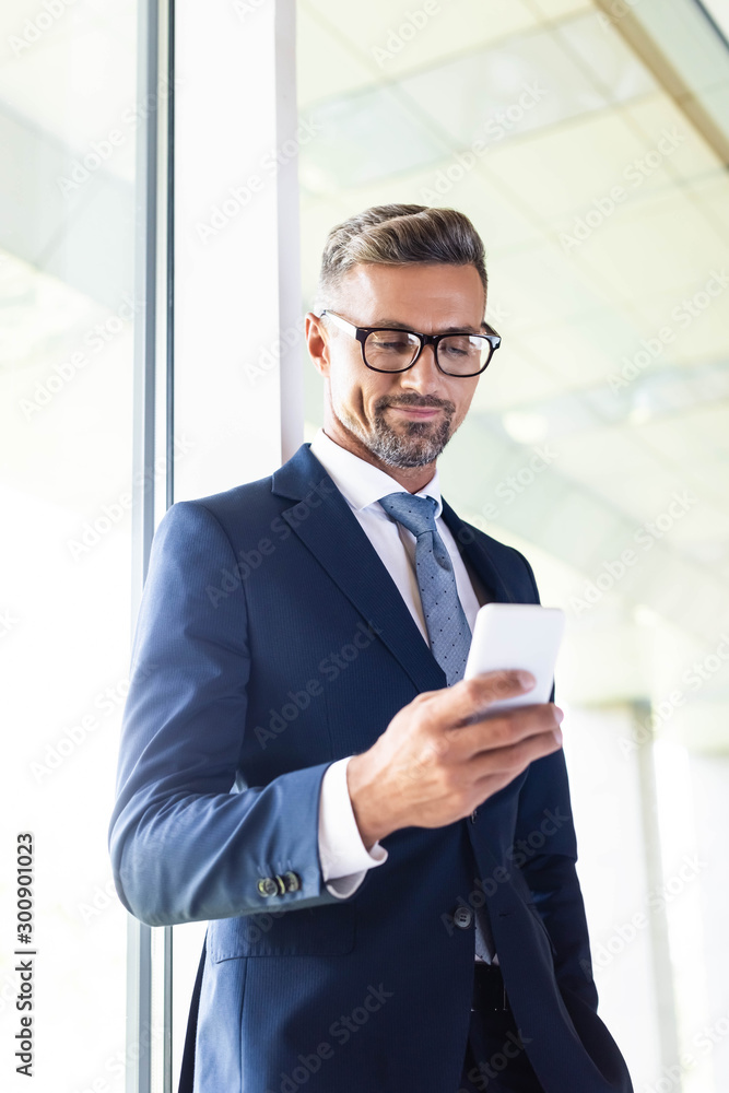 handsome businessman in formal wear and glasses using smartphone